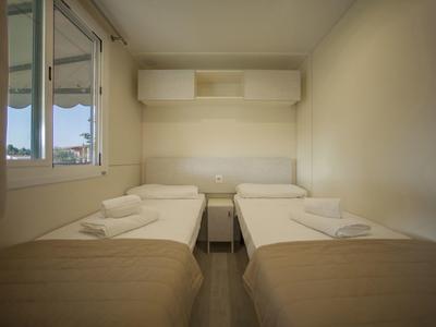 Jednoduchý dvoulůžkový pokoj se dvěma oddělenými postelemi, ručníky a malým nočním stolkem.