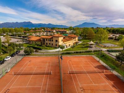 Zwei Tennisplätze aus rotem Sand in einer Anlage mit Gebäuden und Bergen im Hintergrund.