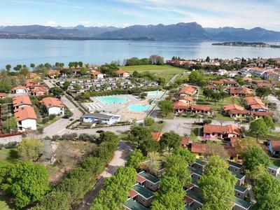 Hotelanlage mit mehreren Gebäuden, Pool und Blick auf einen See und Berge im Hintergrund.