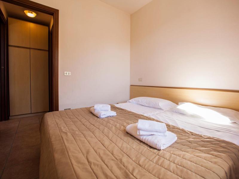 Jednoduchý hotelový pokoj se dvěma jednolůžky, hnědou přikrývkou a bílými ručníky.