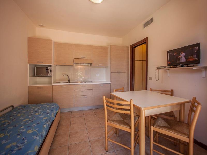 Malý byt s kuchyňským koutem, jídelním stolem, židlemi a pohovkou s modrou matrací.