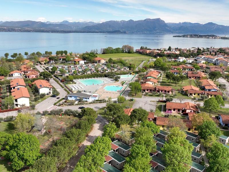 Pohled na rekreační areál s bazény, vilami a jezerem v pozadí za jasného dne.