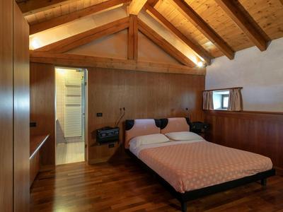 Cozy bedroom with wooden ceiling and simple double bed next to open bathroom access.