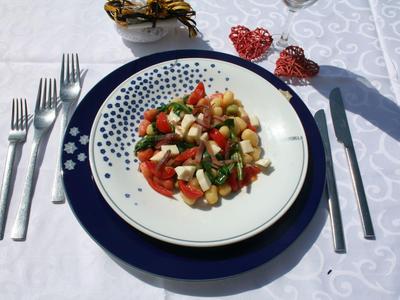 Colorful vegetable salad on white plate with blue charger on white tablecloth