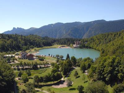 Idyllic lake surrounded by greenery and mountains in the background on a sunny day.