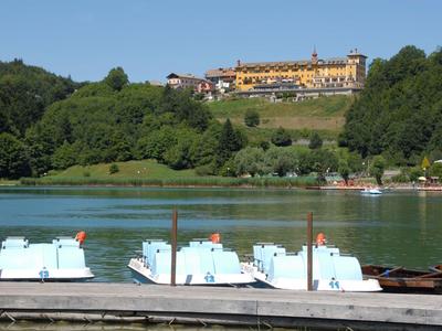 Blick auf einen See mit Tretbooten am Steg und einem großen Hotel auf einem bewaldeten Hügel.