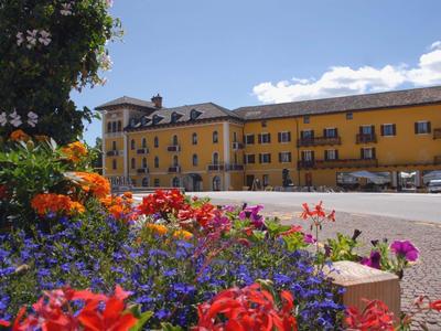 View of yellow hotel building behind colorful flowers under sunny sky.