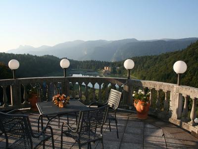 Terrace with seating area and flower decorations overlooking river and forested mountains.