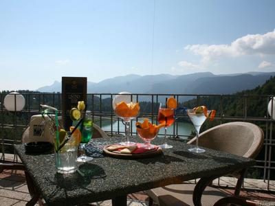 Terrasse mit Tisch und verschiedenen Getränken vor Berg- und Seenlandschaft.