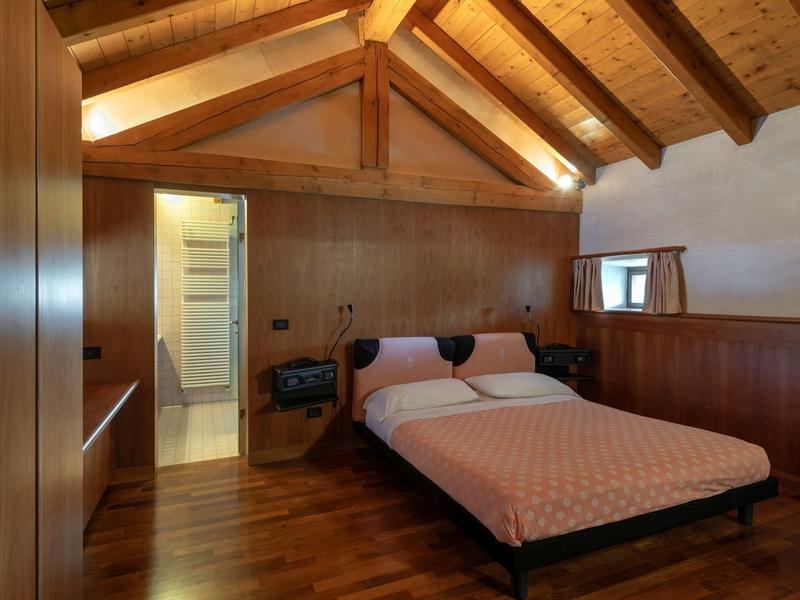 Cozy bedroom with wooden ceiling and simple double bed next to open bathroom access.