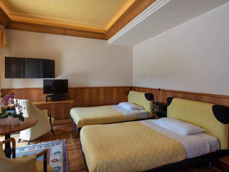 A hotel room with two single beds, a small table, and two TVs mounted on the wall.