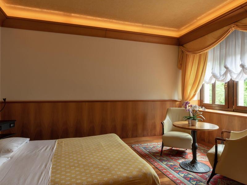 Cozy hotel room with double bed, two chairs, table, and window with curtains.