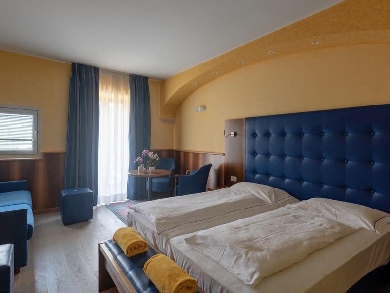 Cozy hotel room with two single beds, blue accents, and a window with curtains.