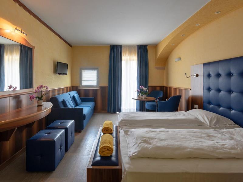 Cozy hotel room with double bed, sofa, TV, and desk in warm tones.