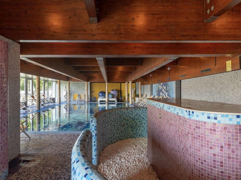 Interior view of an indoor pool with pink and blue tiles and wooden beam ceiling