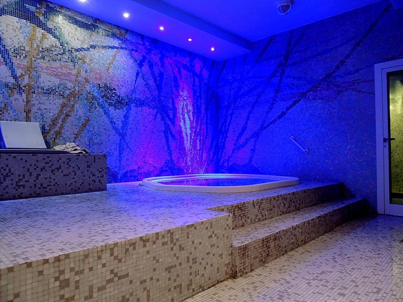 Modern spa area with illuminated hot tub and mosaic tiles in blue and purple tones.