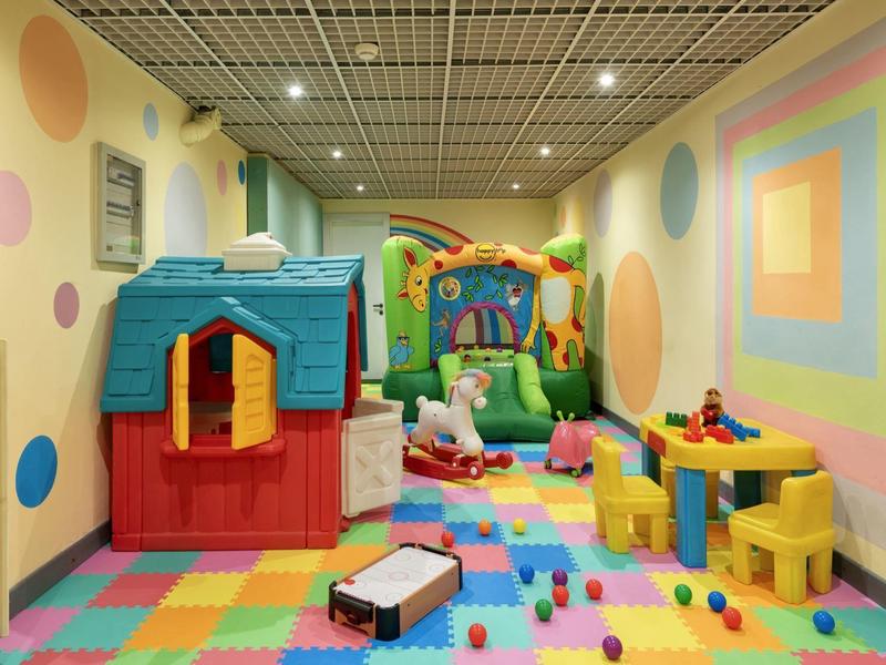 Colorful children's playroom with playhouse, bouncy castle, and toys on colorful floor.