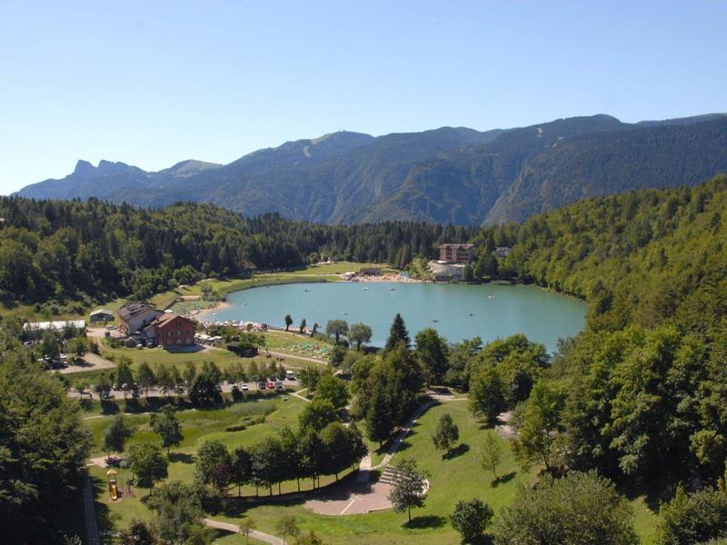 Idyllic lake surrounded by greenery and mountains in the background on a sunny day.