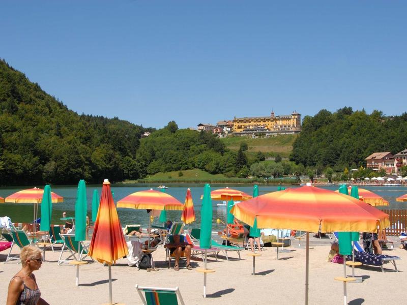 Colorful beach with umbrellas in front of wooded hills and buildings in the background.