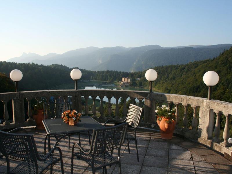 Terrace with seating area and flower decorations overlooking river and forested mountains.