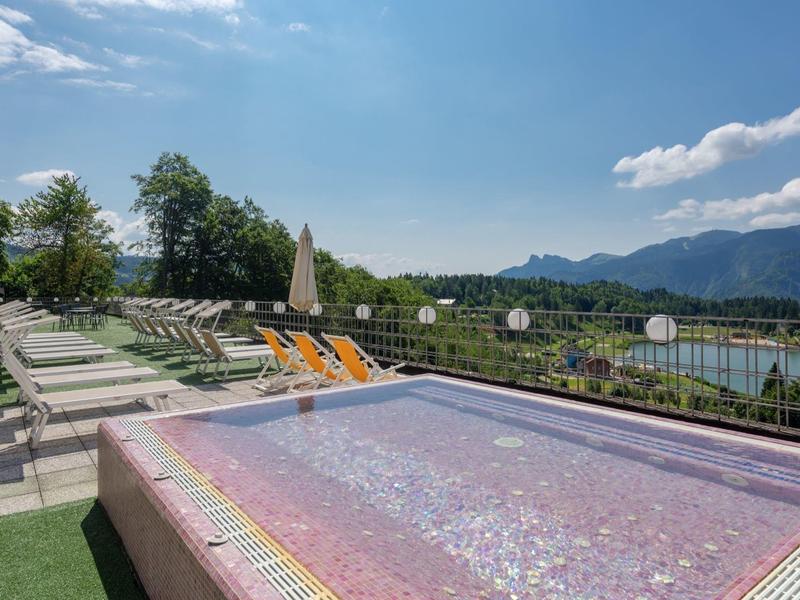 Outdoor pool with lounge chairs, mountain and lake view under a blue sky.
