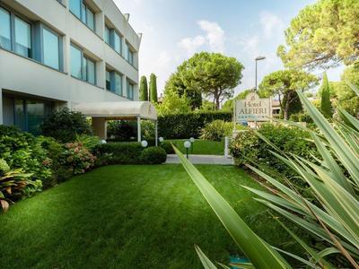 Groene tuin met gras en struiken naast een modern hotelgebouw in zonlicht.