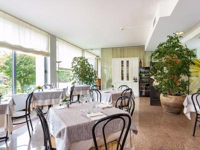 Licht eetkamer met grote ramen, tafels met tafelkleden en planten.