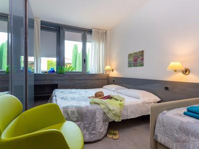 Moderne hotelkamer met twee bedden, een gele fauteuil en grote ramen met uitzicht op groen.