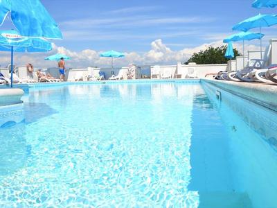 Helderblauw zwembad met blauwe parasols en witte ligstoelen buiten.