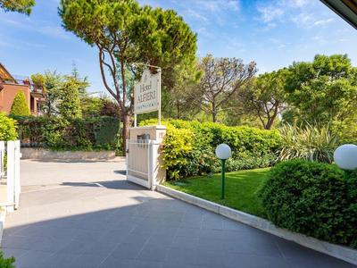 Eingang eines Hotels mit grünem Garten und Bäumen bei sonnigem Himmel.