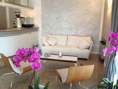 Moderne woonkamer met witte bank, houten stoelen en roze orchideeën in een lichte kamer.