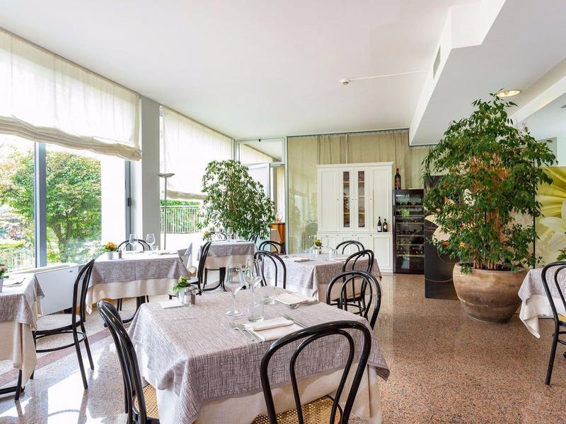 Licht restaurant met grote ramen, witte tafelkleden en zwarte metalen stoelen.