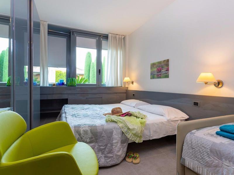 Moderne hotelkamer met twee bedden, een gele fauteuil en grote ramen met uitzicht op groen.