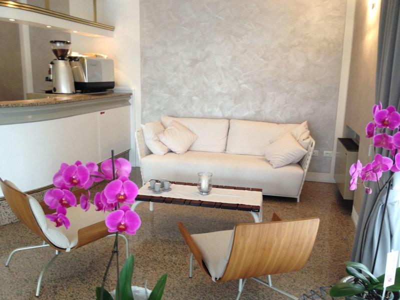 Moderne woonkamer met witte bank, houten stoelen en roze orchideeën in een lichte kamer.