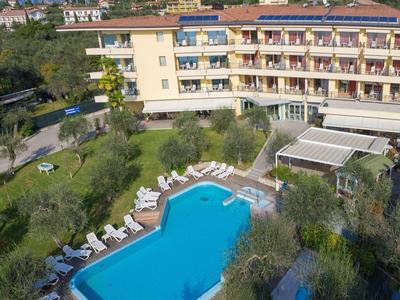 Großes mehrstöckiges Hotel mit gepflastertem Pool, Liegestühlen und viel grüner Vegetation.