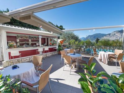 Terrasse mit Tischen, Stühlen und Bar, umgeben von Bergen und blauem Himmel.