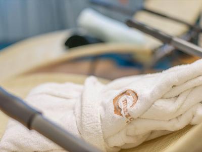 Weicher, weißer Bademantel mit braunem Logo liegt gefaltet auf einem Holzkinderwagen.