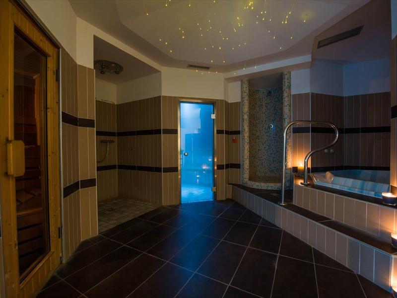 Moderner Wellnessraum mit Sauna, Whirlpool, Kerzenlicht und Sternenhimmel-Deckenbeleuchtung.