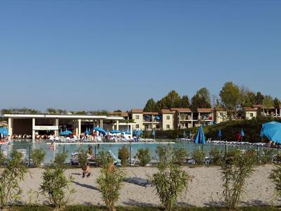 Großer Schwimmbadbereich mit Liegestühlen, Sonnenschirmen und mehreren Gebäuden im Hintergrund.
