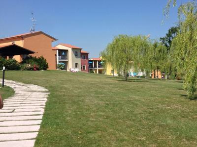 Grüner Rasen mit Gehweg und bunten Häusern unter klarem blauem Himmel an einem sonnigen Tag.