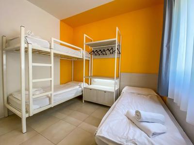 Hotelzimmer mit Etagenbett, Einzelbett, gelber Wand und blauen Vorhängen.