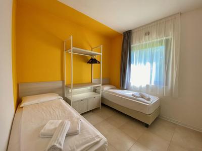 Modernes Hotelzimmer mit zwei Einzelbetten, offenem Kleiderständer und gelber Wand.