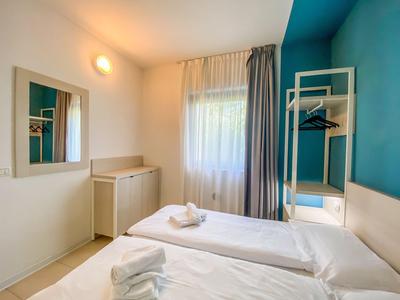 Helles Hotelzimmer mit zwei Einzelbetten, weißen Vorhängen und blauer Akzentwand.