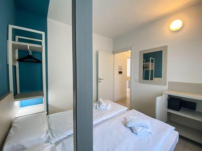 Hell eingerichtetes Hotelzimmer mit zwei Einzelbetten, weißen Bettwäsche und einem Spiegel an der Wand.