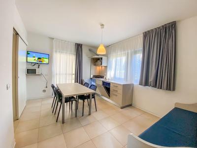 Helles, modernes Hotelzimmer mit Essbereich und kleiner Küche, große Fenster mit Vorhängen.