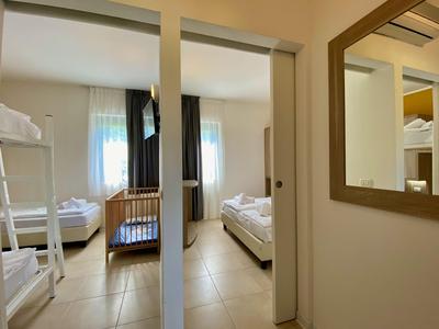 Helles Hotelzimmer mit Stockbett, Einzelbett, Kinderbett und großem Spiegel.