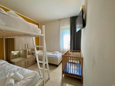 Kleines Hotelzimmer mit Etagenbett, Einzelbett und Kinderbett neben Fenster.