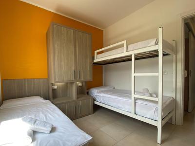 Kleines Hotelzimmer mit Etagenbett, Einzelbett, oranger Wand und grauen Möbeln.