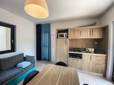 Gemütliche Hotelküche mit Holzschränken, Kühlschrank, Mikrowelle und blauem Vorhang neben Sofa.
