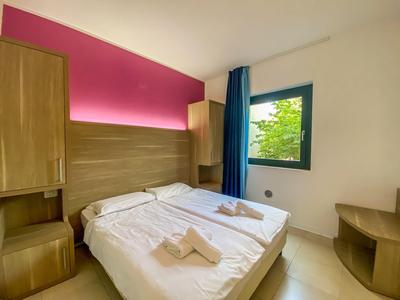 Hell eingerichtetes Hotelzimmer mit Doppelbett, Holzmöbeln und Fenster mit Blick ins Grüne.
